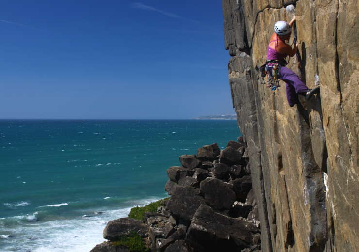Inma Garrido aparece a la derecha de la foto escalando en una pared vertical. Al pie de vía se ven rocas y el mar que también ocupa toda la parte izquierda de la foto. Está tomada en Portugal en Casal de Pianos y el crédito de la foto es de Iván Jara