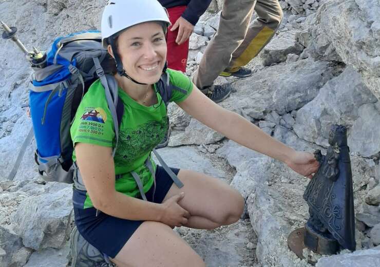 Elena Arienza aparece en primer plano en cuclillas, en la Cumbre del Torrecerredo (techo de los Picos de Europa). Lleva un casco blanco, una camiseta verde y una mochila azul a su espalda. Tiene una gran sonrisa y un brillo especial sus ojos verdes.