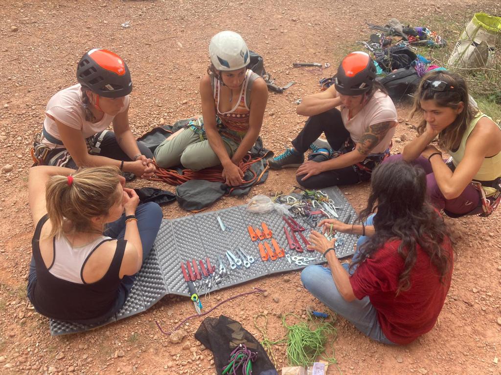 Seis alpinistas del equipo sentadas en círculo en el suelo prestan atención a las explicaciones de la instructora acerca del material de escalada. 