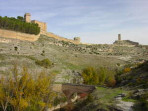 Fotografía que presenta un fragmento del sendero cuando cruza el río Júcar en un meandro encajado. En la parte superior se visualiza el castillo de Alarcón.