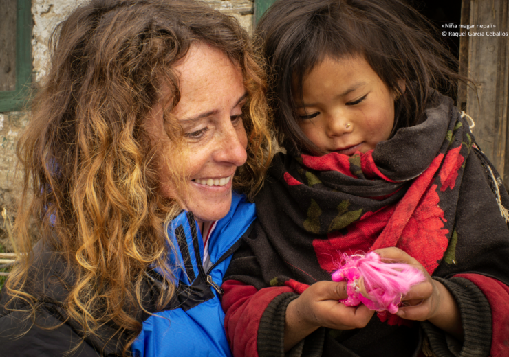 Raquel aparece a la izquierda de la foto sosteniendo a una niña nepalí que aparece a la derecha y tiene una muñeca en la mano. Es un primer plano y ambas sonríen observando la muñeca.