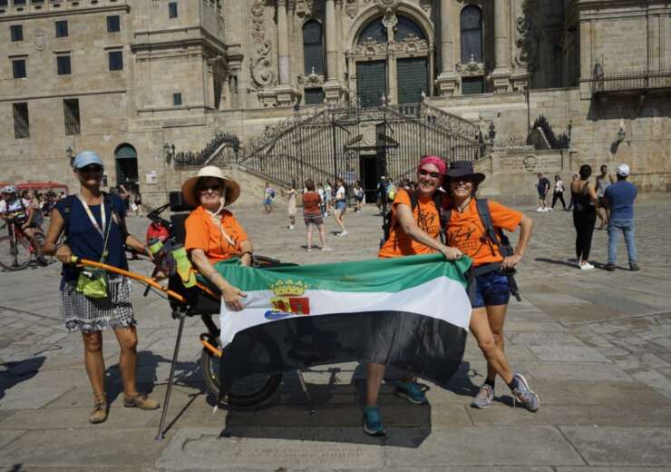En la imagen se puede ver a Yolanda Álvarez, en la plaza del Obradoiro, frente a la Catedral de Santiago de Compostela. Está montada en una silla Joëlette y posa, exhibiendo la bandera de Extremadura (su tierra), junto a una parte del equipo de pilotos que hicieron posible su Camino de Santiago.