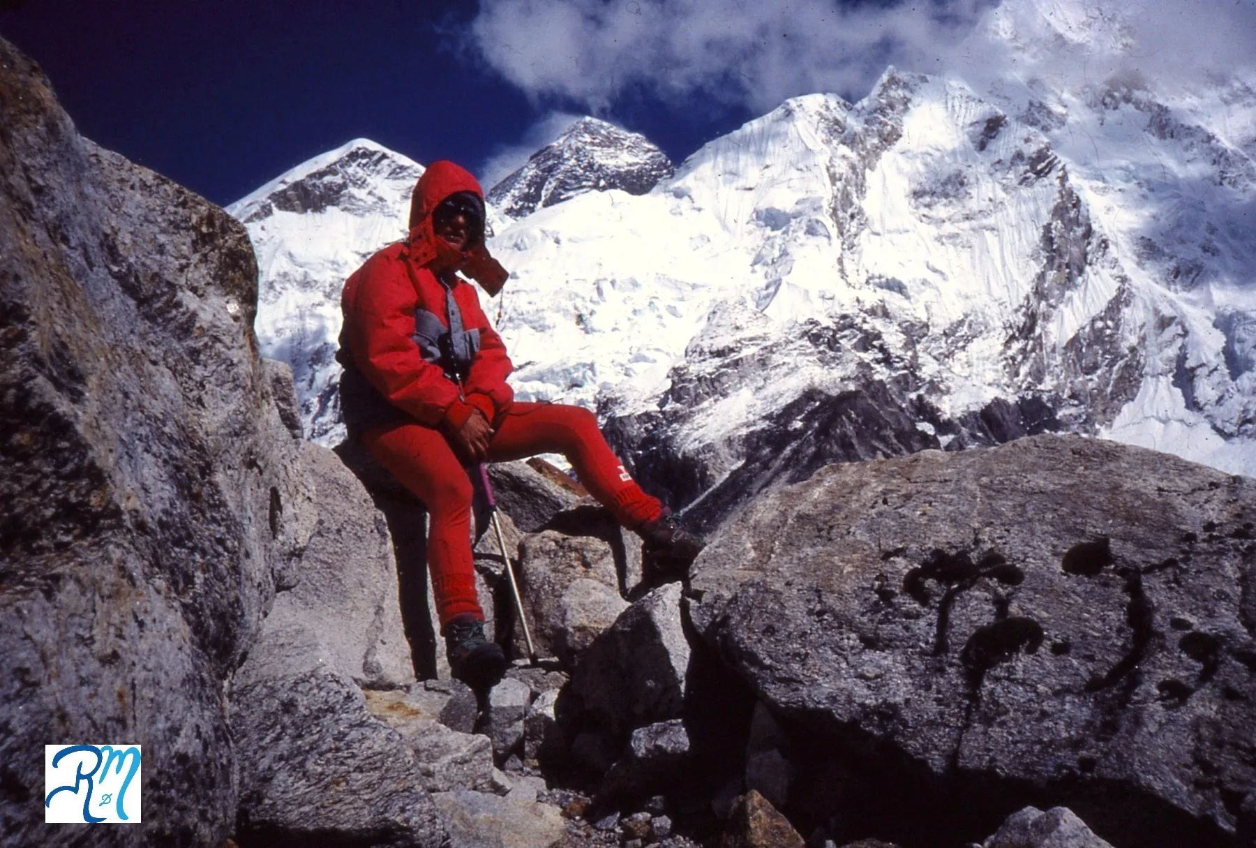 Reyes aparece sentada en unas grandes rocas con ropa de alta montaña roja, cubierta cabeza con capucha y gafas de nieve. Tras ella tres de las grandes montañas del Himalaya: Everest, Nuptse y Lhotse