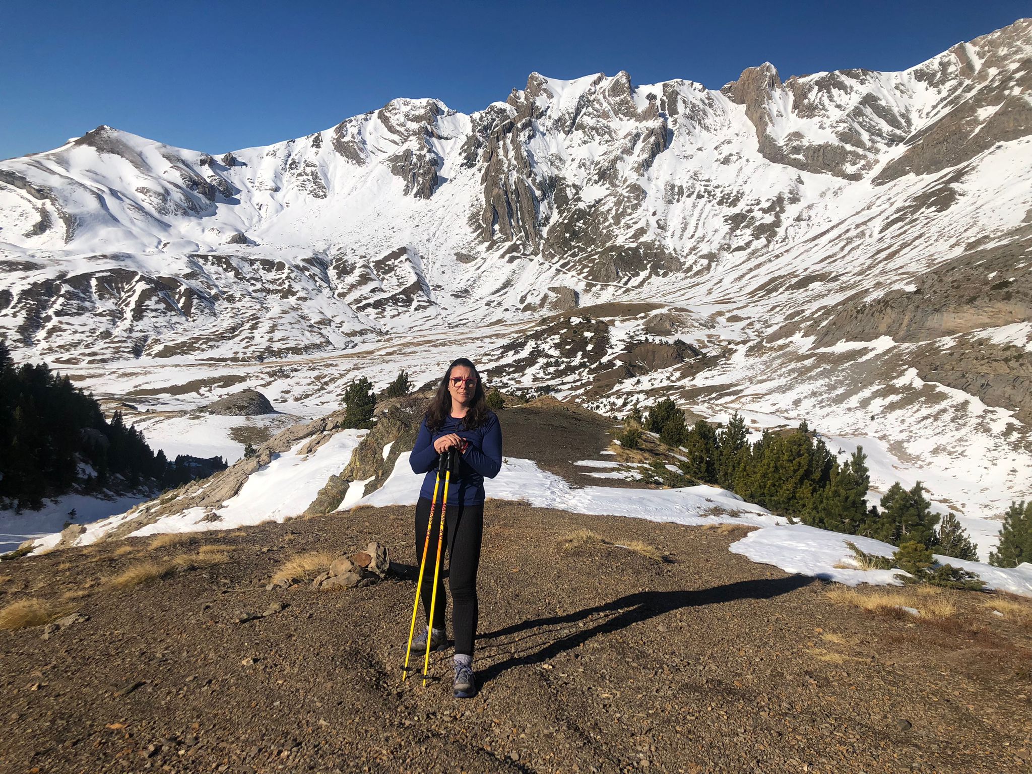 Celia se encuentra de pie, en primer plano, haciendo senderismo en la cabecera del valle de Tena, sobre Sallent de Gállego (Huesca). Al fondo la Peña Foratata cubierta de nieve."
